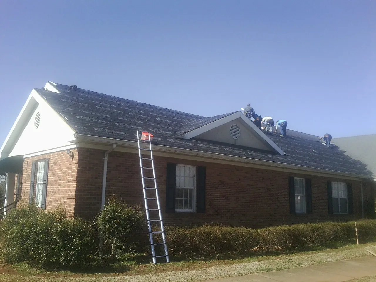 Crew tearing shingles off a brick ranch roof with a ladder set — Emergency Roof Repair work by our crew in Carlisle