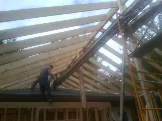 Rafters going up over a new addition with a worker on the wall in Carlisle