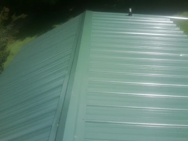 New green metal panels meeting at the ridge of a roof — Flat Roof Repair work by our crew in Carlisle